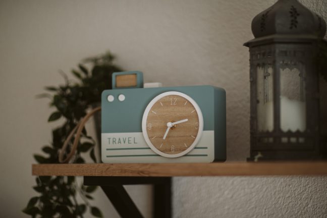 Blue and grey clock sitting on a shelf with a plant in the background
