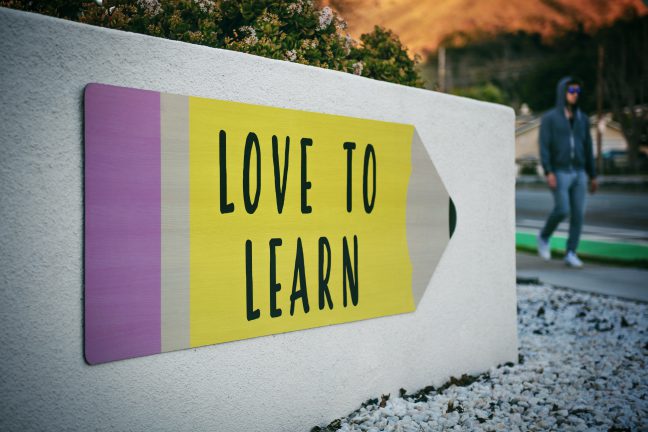 Love to learn pencil shaped sign on a wall near a walking man